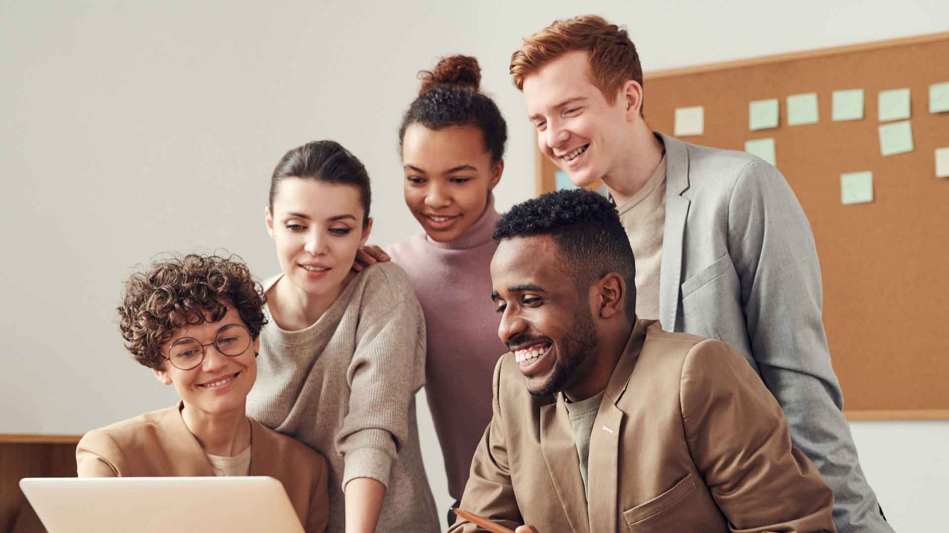 Five people smiling looking over the laptop screen.